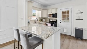 A modern kitchen with white cabinetry, a granite island, and a black trash bin. - Carriage Manor- Right next to the  Fountain of Youth & Beach.
Pets are welcomed! (St. Augustine)