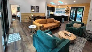 A modern living room with a sofa, armchairs, and a coffee table. There is a dining area with a table and chairs, and a kitchen with a sink and stove. - Modern Mountain Getaway with hot tub & fire pit 10 minutes to Helen (White County)
