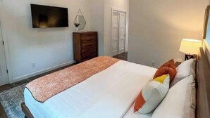 A bedroom with a bed, a dresser, a TV mounted on the wall, and a door in the background. - Modern Mountain Getaway with hot tub & fire pit 10 minutes to Helen (White County)