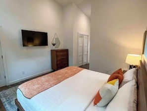 Een slaapkamer met een bed, een dressoir, een aan de muur bevestigde televisie en een deur op de achtergrond.