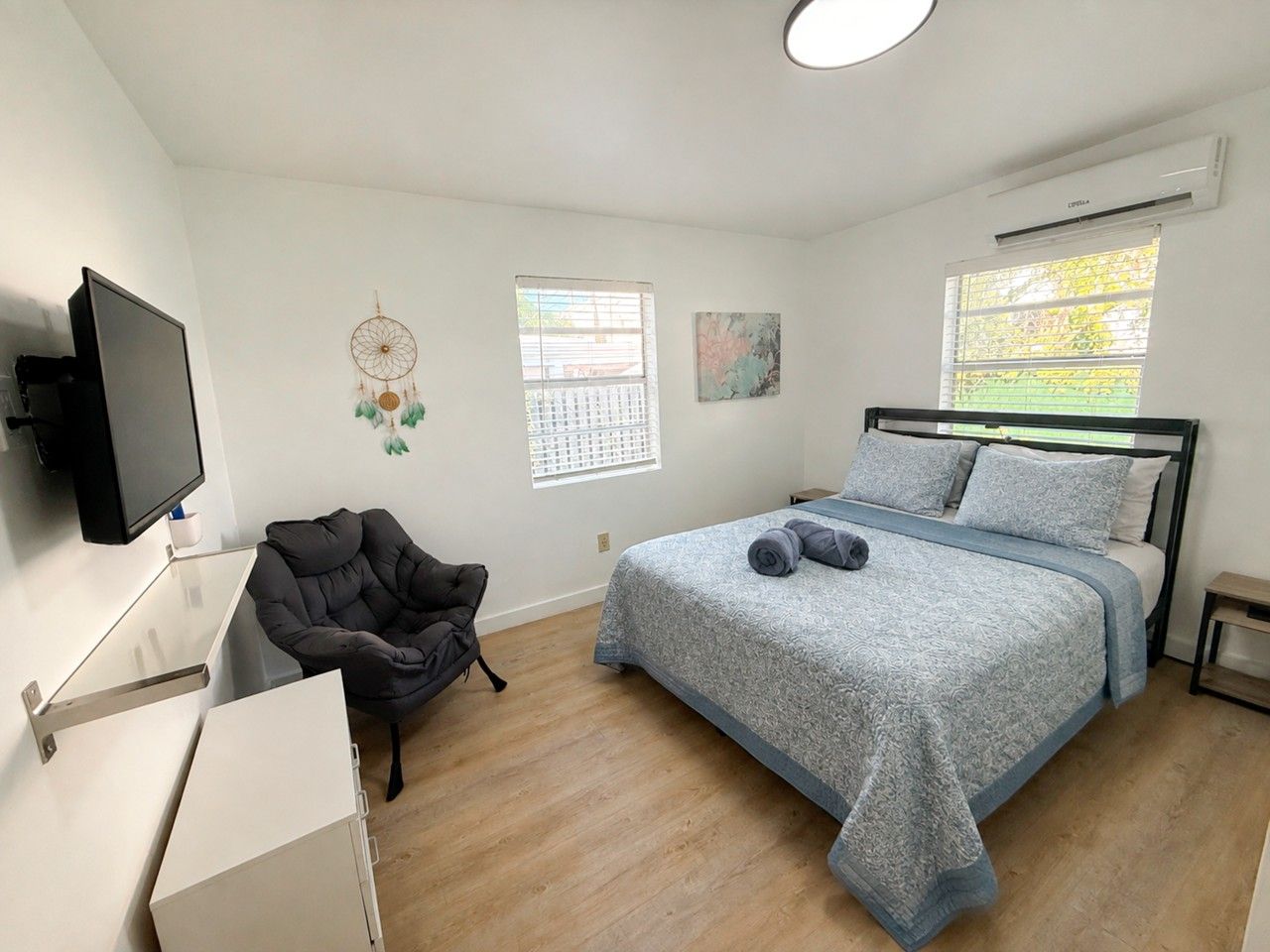 Un dormitorio con cama, una silla, un televisor y una ventana.
