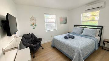 Un dormitorio con cama, una silla, un televisor y una ventana.