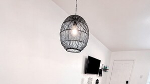 Moderni olohuone, jossa on pyöreä valkoinen pöytä, valkoiset tuolit, musta pallomainen riippuvalaisin, seinälle asennettu litteänäyttöinen televisio ja kuviollinen matto.