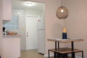 Uma cozinha com geladeira, uma mesa de jantar com xícaras empilhadas e um lustre.