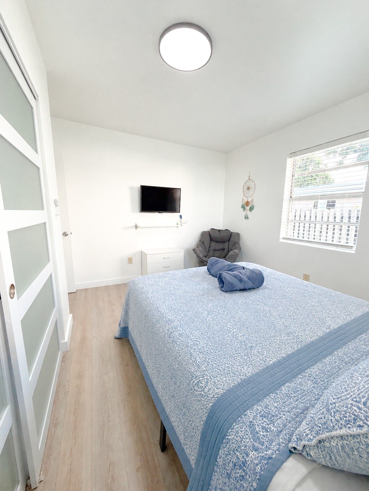 A bedroom with a bed, a television, a chair, a window, and a door.