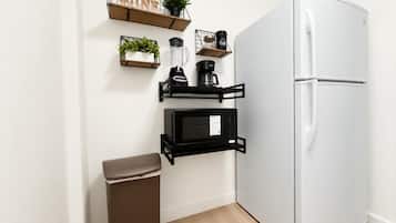 Una cocina compacta con un refrigerador blanco, un microondas y un cubo de basura.