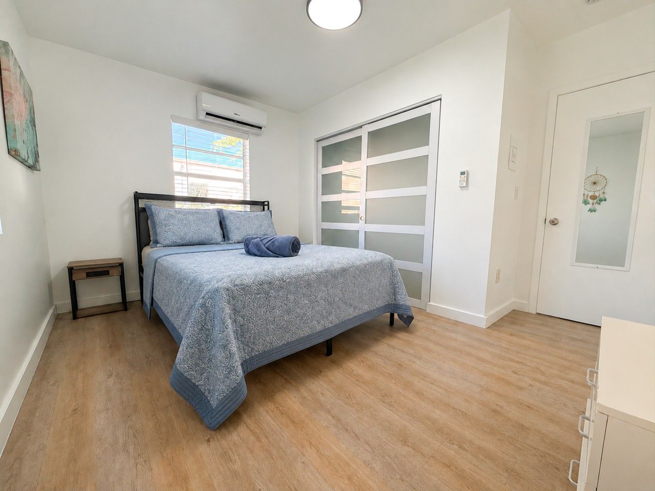 A bedroom with a bed, a nightstand, a wardrobe, and a window with blinds.