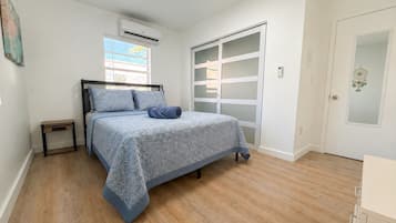 Un dormitorio con cama, mesita de noche, armario y ventana con persianas.