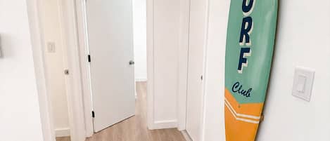 A hallway with a surfboard on the wall, wooden flooring, and white doors.