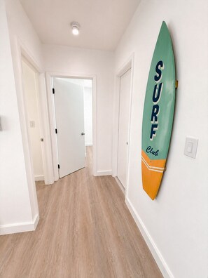 Un couloir avec une planche de surf accrochée au mur, un plancher en bois et des portes blanches.