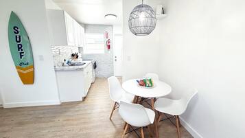Una cocina moderna con armarios blancos, una zona de comedor con sillas blancas y una decoración de tabla de surf en la pared.