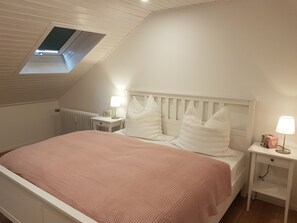 A bedroom with a sloped ceiling, a skylight, a bed with white bedding, two bedside tables with lamps, and a radiator. - Vacation apartment Schwarzwaldblick in Lenzkirch (incl. HSC) (Lenzkirch)