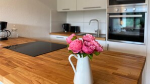 A modern kitchen with white cabinets, a wooden countertop, a coffee maker, and a vase with pink flowers.
