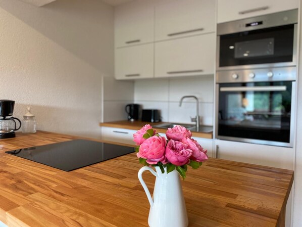 Ett modernt kök med vita skåp, en träbänkskiva, en kaffebryggare och en vas med rosa blommor.