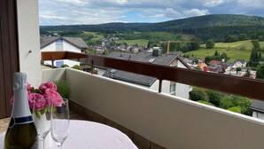 A balcony with a table set for two, overlooking a village and hills.