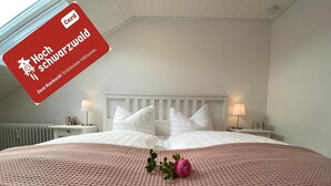 A hotel room with a large bed, white bedding, and a pink textured rug. There are two bedside tables with lamps and a framed picture on each.
