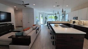 A modern kitchen with a central island, dark cabinetry, and a flat-screen TV. - Desert Modern 4BR: Pool, Spa & Mtn views #259142 (La Quinta)