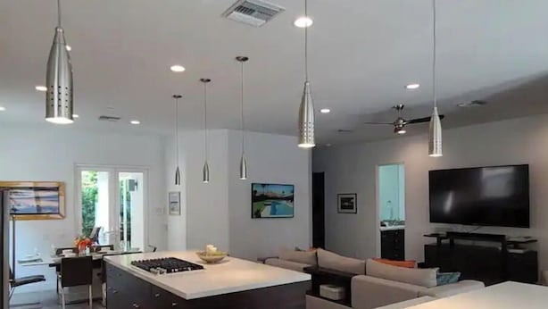 A modern kitchen with a central island, pendant lighting, and a flat-screen TV mounted on the wall. - Desert Modern 4BR: Pool, Spa & Mtn views #259142 (La Quinta)