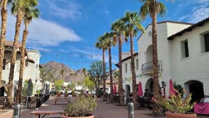 A plaza with palm trees, outdoor seating, and buildings with arched windows. - Desert Modern 4BR: Pool, Spa & Mtn views #259142 (La Quinta)