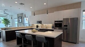 A modern kitchen with a large island, stainless steel appliances, and pendant lighting. - Desert Modern 4BR: Pool, Spa & Mtn views #259142 (La Quinta)