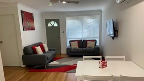 Ein Wohnzimmer mit zwei Sofas, einem Esstisch mit Stühlen, einem roten Teppich und einem Deckenventilator.