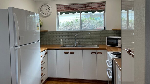 Eine moderne Küche mit weißen Schränken, einer Edelstahlspüle, einer Mikrowelle und einem Kühlschrank.