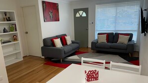 Ein modernes Wohnzimmer mit zwei grauen Sofas, einem weißen Esstisch und einem rot-grauen Teppich.
