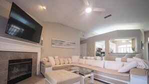 A modern living room with a sectional sofa, a glass coffee table, a fireplace, and a flat-screen TV mounted above it. - Super Clean Fantastic Pool Home Near Everything (Orange Park)