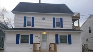 Une maison à deux étages avec un porche à l’avant, un petit balcon et le numéro « 15 » bien visible sur la porte.