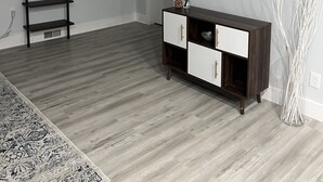 Un salon moderne avec un plancher en bois, un meuble en bois foncé doté de tiroirs blancs, un téléviseur à écran plat fixé au mur, une étagère décorative avec une plante et un tapis à motifs.