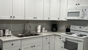 Une cuisine moderne avec des meubles blancs, un évier en acier inoxydable, un four à micro-ondes, une machine à café et un four.