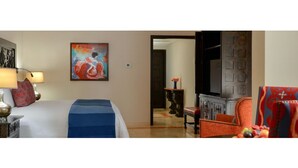 Una habitación de hotel con cama, una silla, un cuadro y televisor.