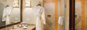 Un baño con tocador, cabina de ducha con mampara de vidrio y dos albornoces blancos colgados en ganchos.