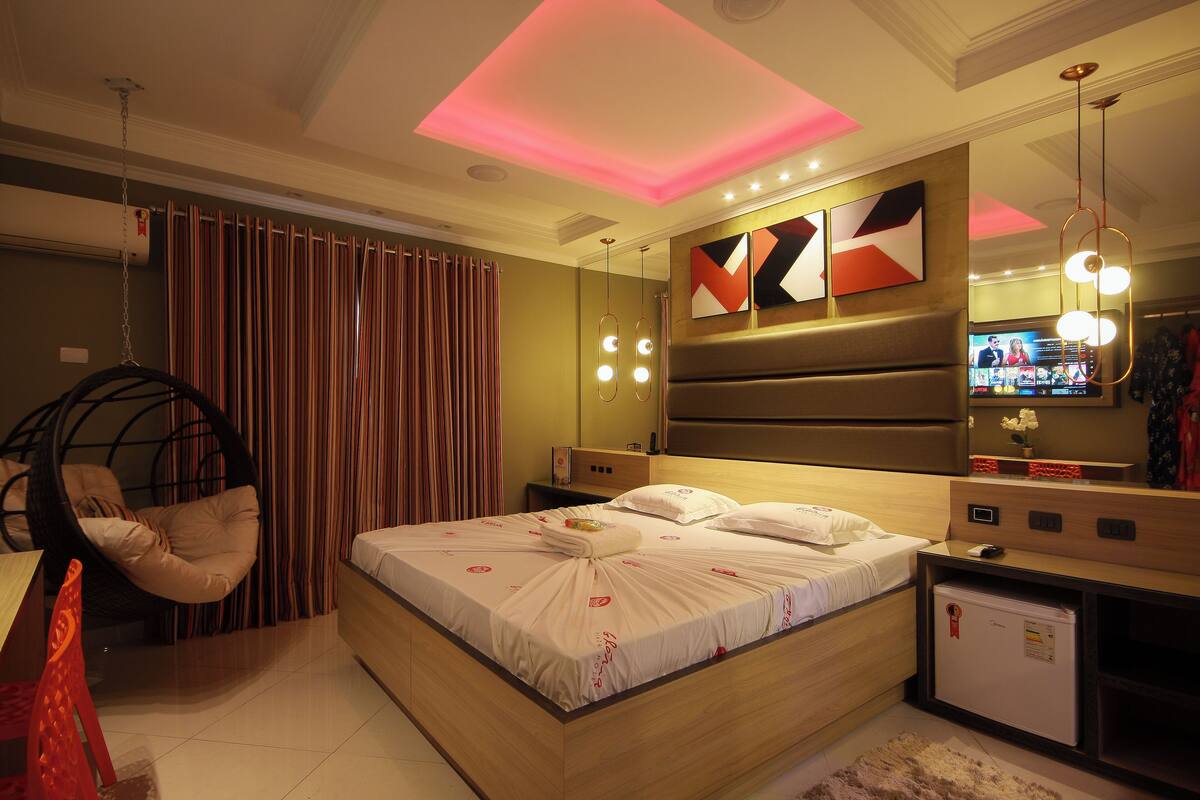 A modern hotel room with a large bed, a hanging chair, a small desk, and a television.