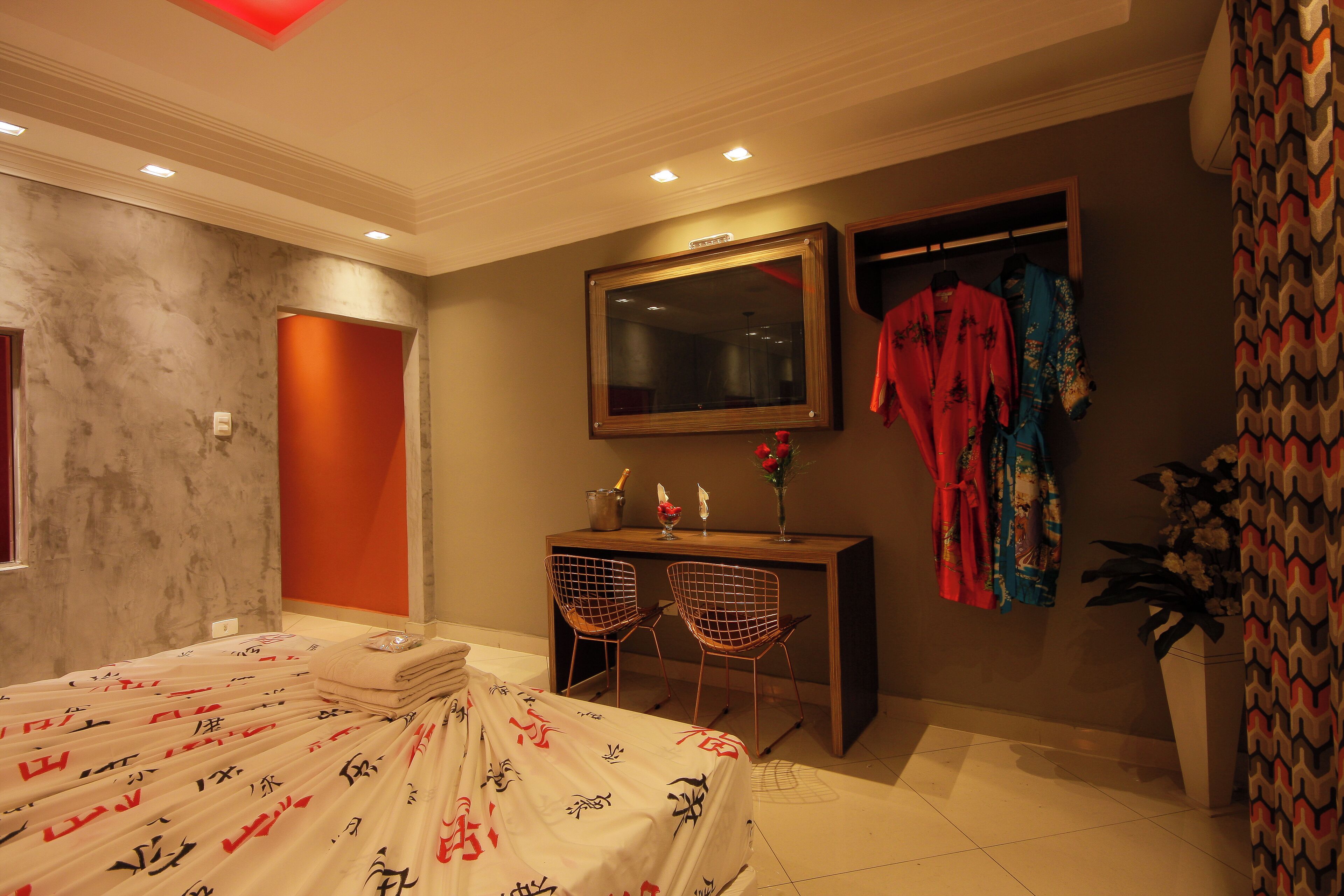 A hotel room with a bed, a desk with chairs, a mirror, and a window with curtains.