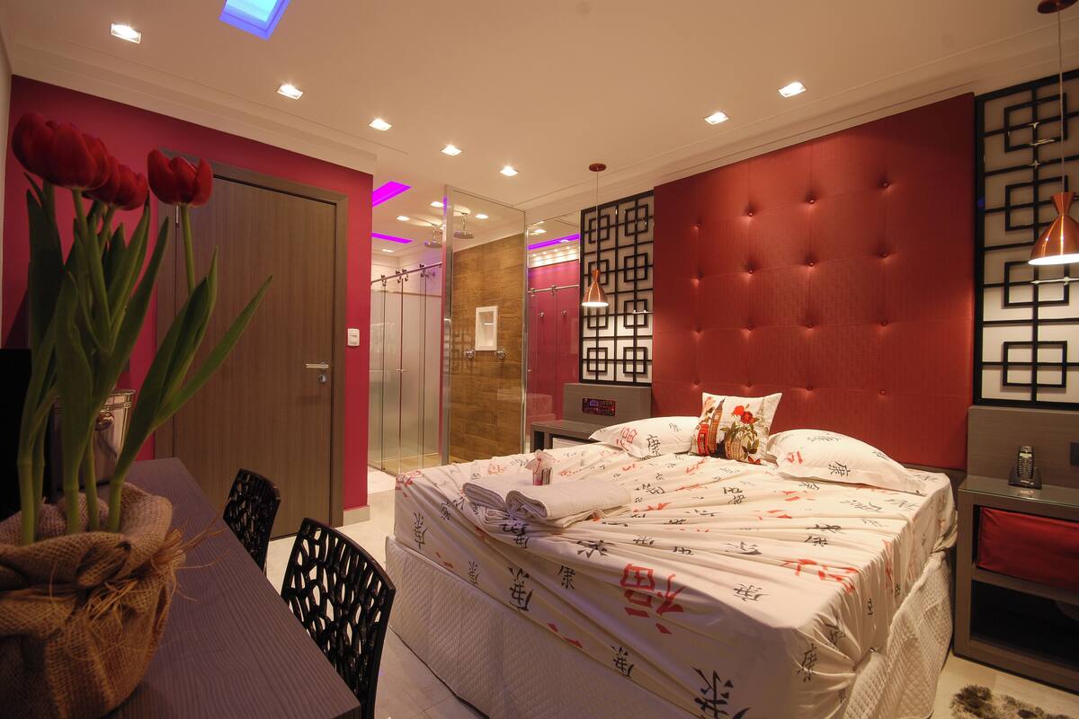 A modern bedroom with a large bed, a wooden door, and a red accent wall.