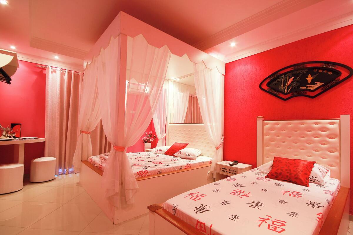 A bedroom with two beds, a red accent wall, and a canopy bed.