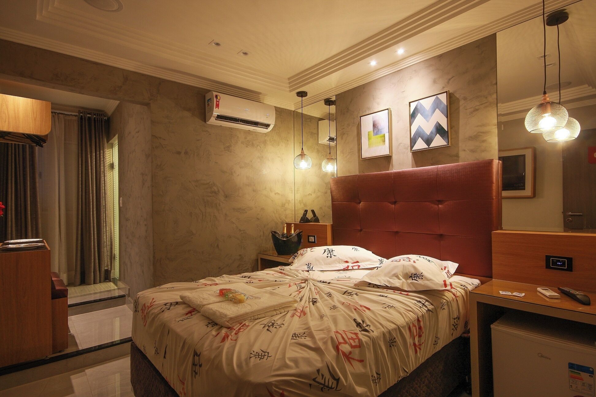 A hotel room with a bed, bedside table, and a desk with a computer.