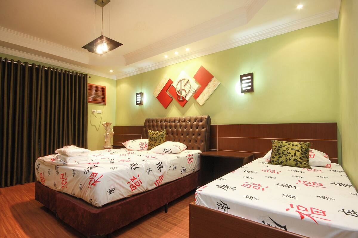 A hotel room with two beds, a large window with curtains, a wall-mounted light, and a decorative wall piece.