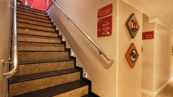 A staircase with black steps and a metal handrail, leading to a red wall with directional signs.