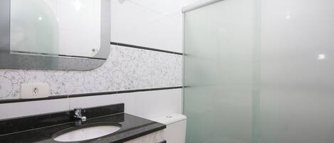 Une salle de bain avec un lavabo blanc, un plan de toilette noir et une cabine de douche en verre.