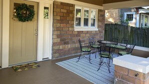 Une terrasse couverte avec un mur en briques, une porte ornée d’une guirlande et une table entourée de chaises.