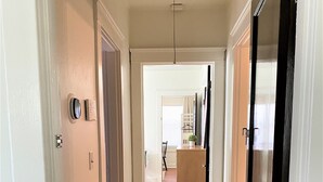 Un couloir doté d’un plancher en bois, de murs blancs et d’une porte donnant sur un espace cuisine.