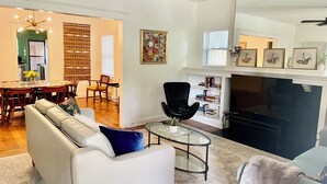 Un salon comprenant un canapé, une table basse en verre, un fauteuil noir, une cheminée et un coin repas avec une table et des chaises.