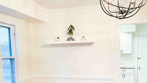 Un coin repas avec une table à carreaux noirs et blancs, des chaises noires, un lustre et un mur blanc orné d’étagères.