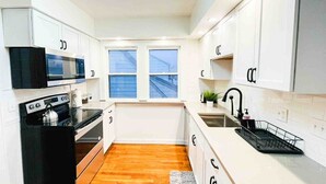 Une cuisine moderne avec des meubles blancs, une cuisinière noire, un four à micro-ondes et une fenêtre donnant sur l’extérieur.