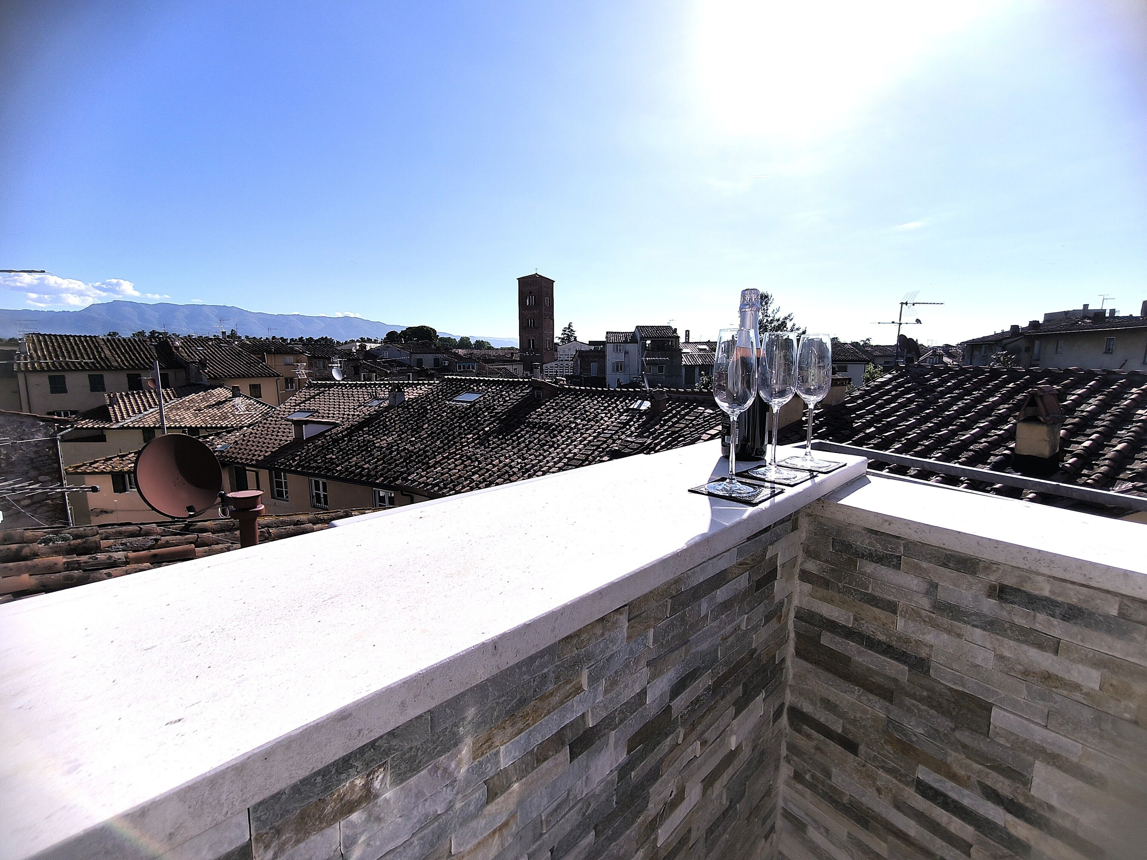 Eine Dachterrasse mit einer Steinmauer, einer großen Satellitenschüssel und drei leeren Weingläsern.