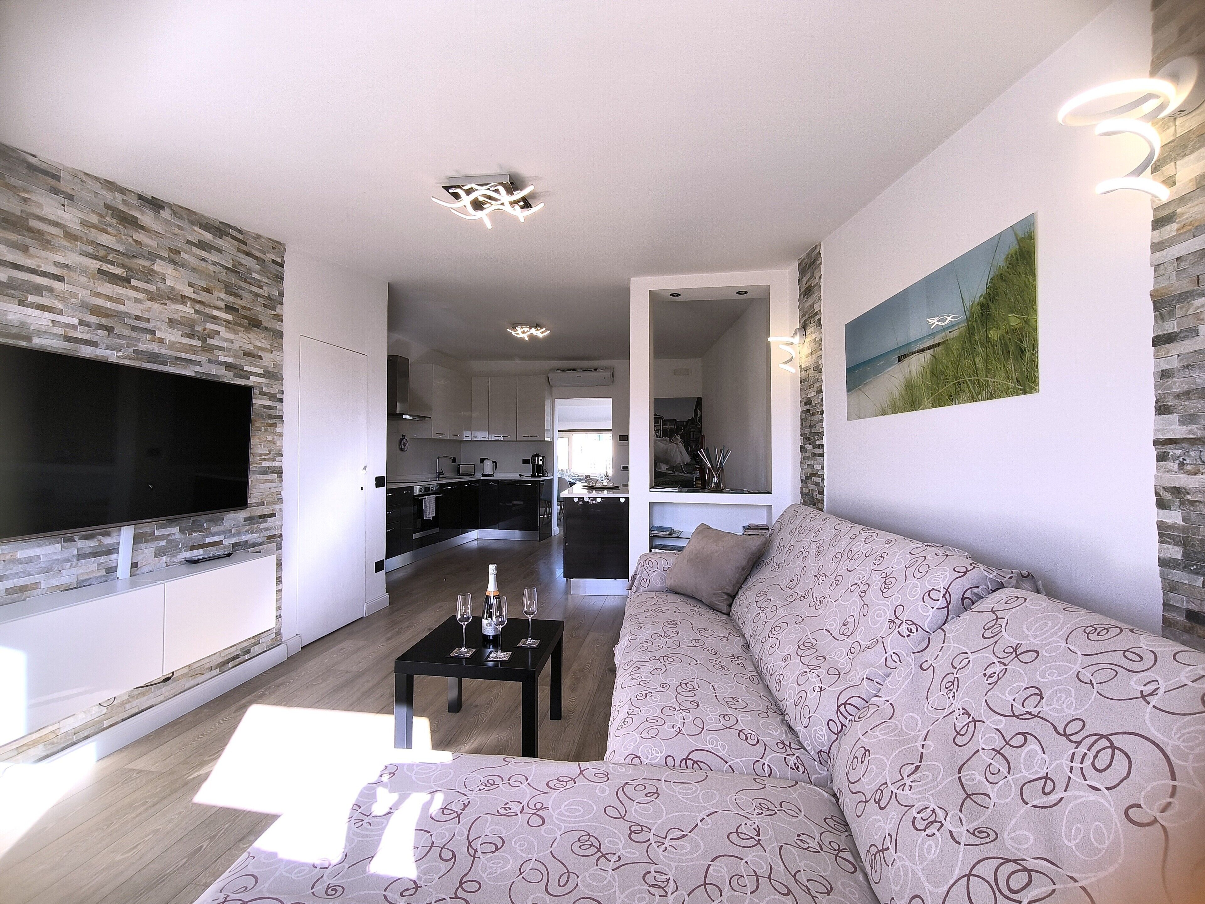 A modern living room with a flat-screen TV, a patterned sofa, and a dining area with a table set for four.