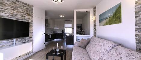 A modern living room with a flat-screen TV, a patterned sofa, and a dining area with a table set for four.