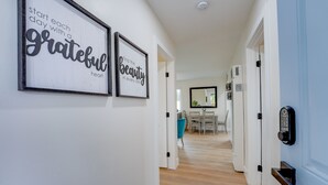 Een hal met geïnspireerde citaten in lijsten aan de muur, een eethoek op de achtergrond, en een moderne deur met cijferslot.
